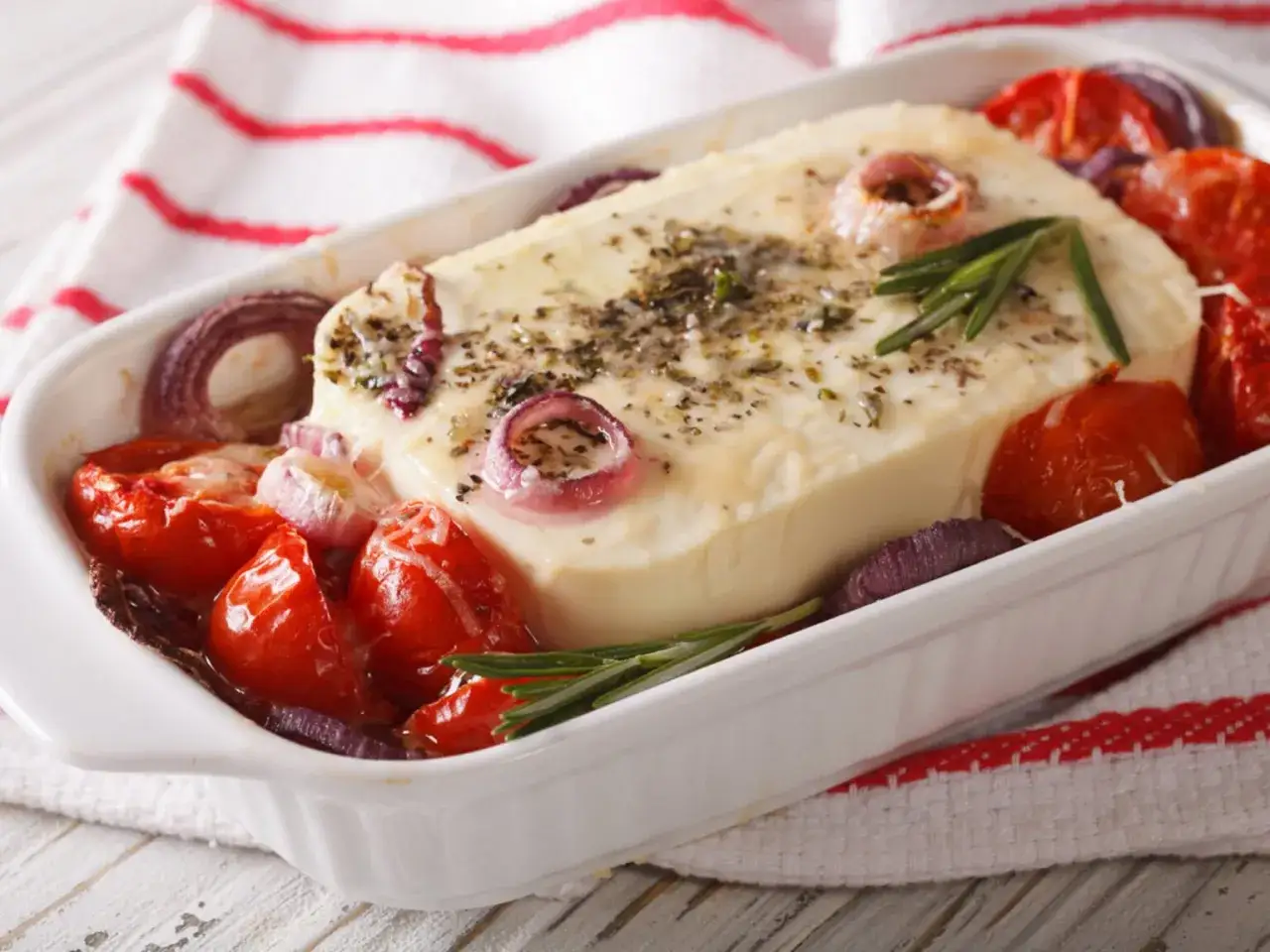Ein Block gebackener Feta mit Kirschtomaten und roten Zwiebeln, garniert mit Rosmarin.