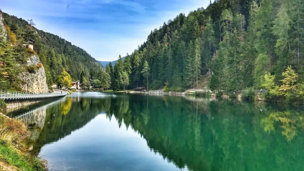 Un lago smeraldo con una spiaggia tranquilla, circondato da foreste lussureggianti e montagne.