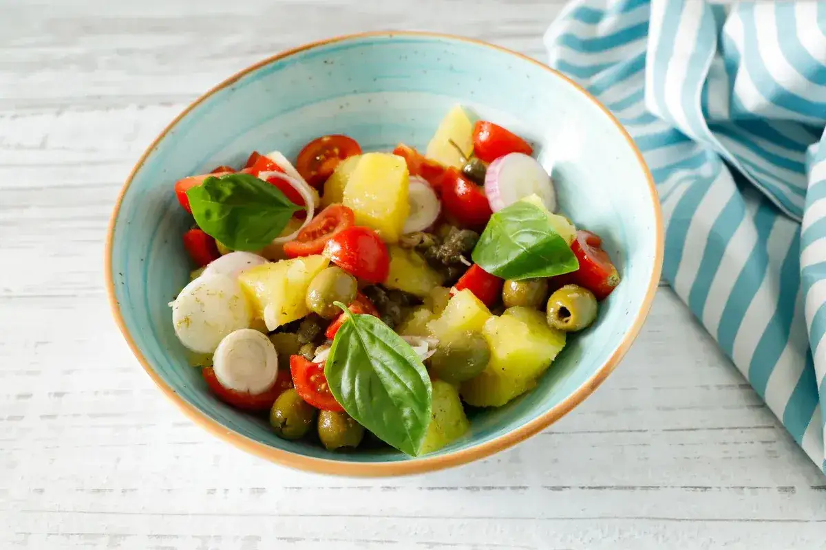 Insalata pantesca in ciotola azzurra: patate, pomodorini, olive, capperi e basilico fresco, un tripudio di sapori mediterranei.