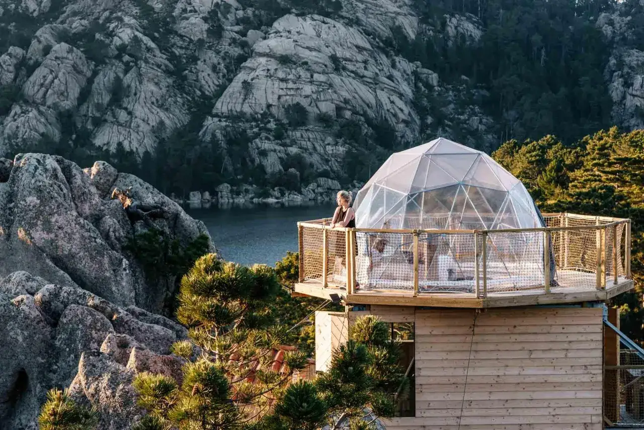 Un logement insolite montagne avec une bulle transparente offrant une vue imprenable sur un lac et des rochers escarpés.