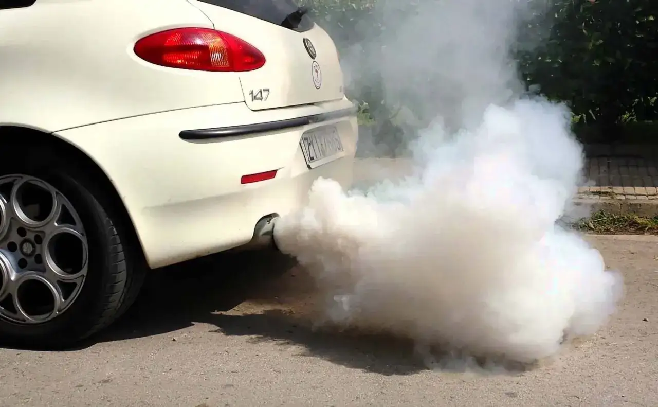 Fumata bianca auto: un'Alfa Romeo 147 emette un denso fumo bianco dallo scarico, creando una nuvola densa.