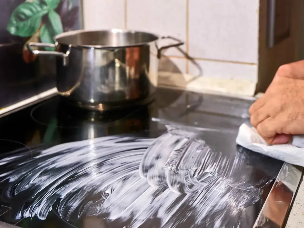 Se puede limpiar la placa de inducción con vitroclen. Una mano frota con un paño blanco la superficie negra, dejando un rastro de espuma.