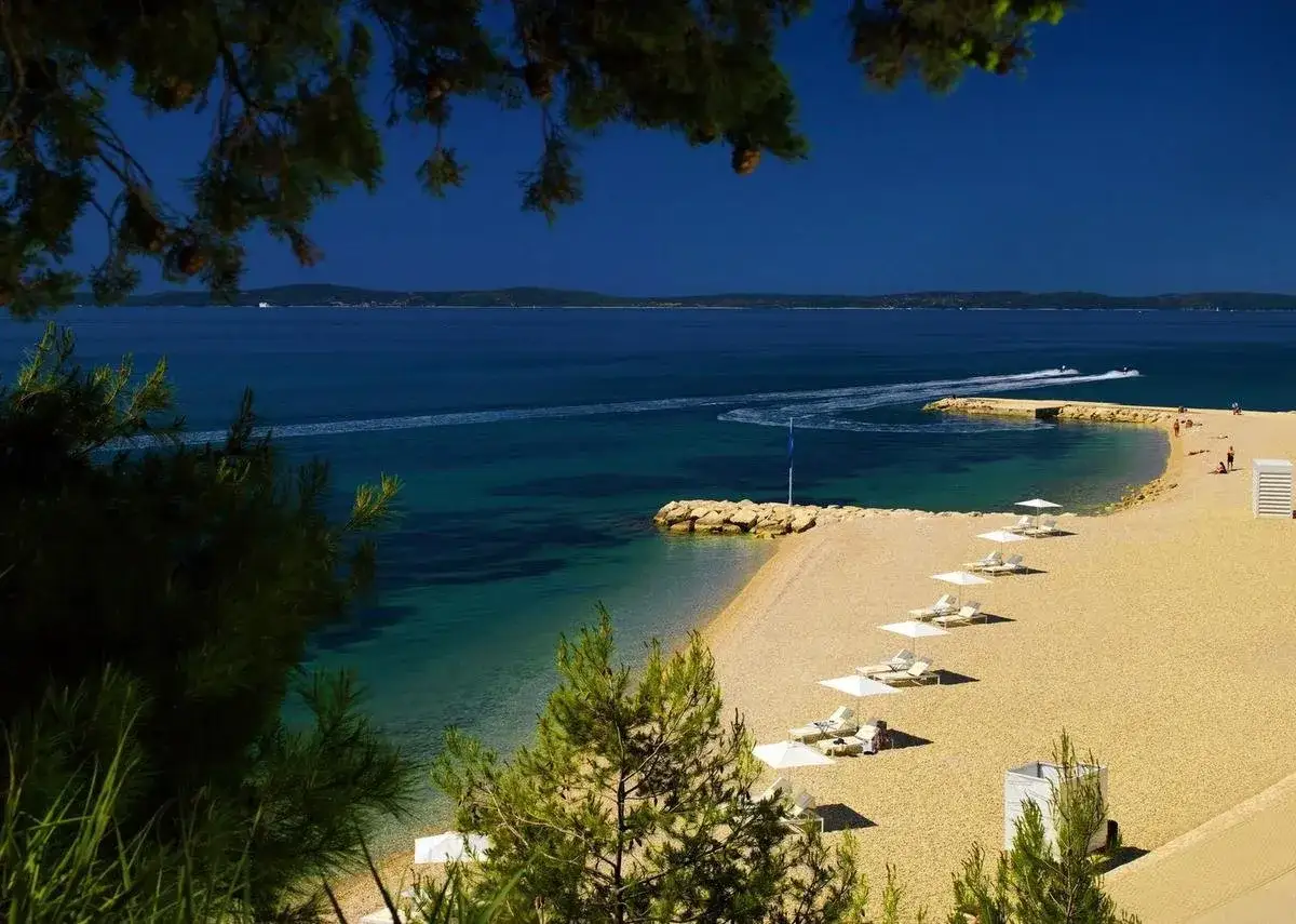Piękna plaża z leżakami i parasolami, idealna na relaks przy hotelu Radisson Blu Split. Woda kusi błękitem, a łodzie wodne dodają dynamiki.