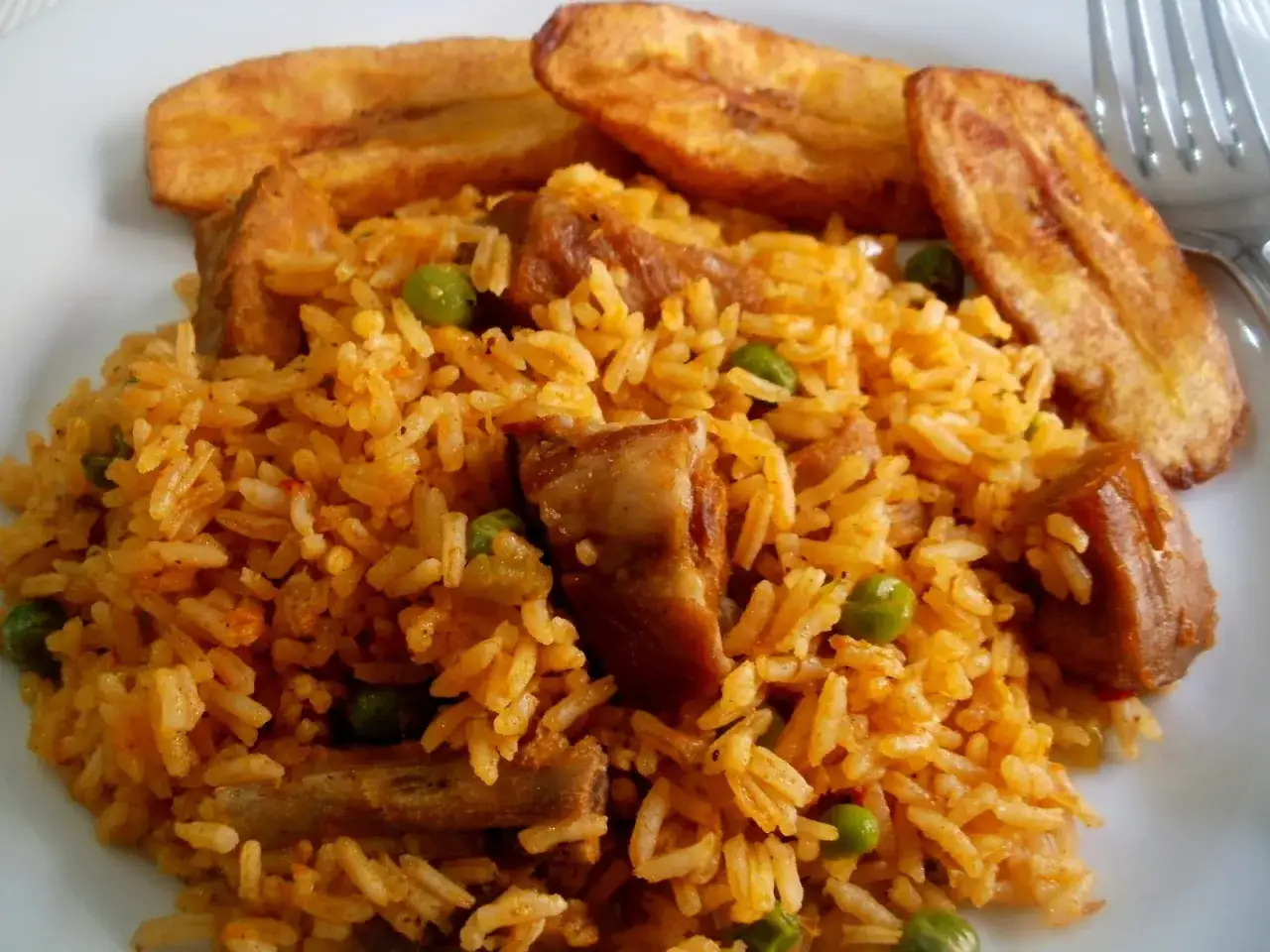 Delicioso arroz con costillas, guisantes y pl&aacute;tanos fritos en un plato blanco.