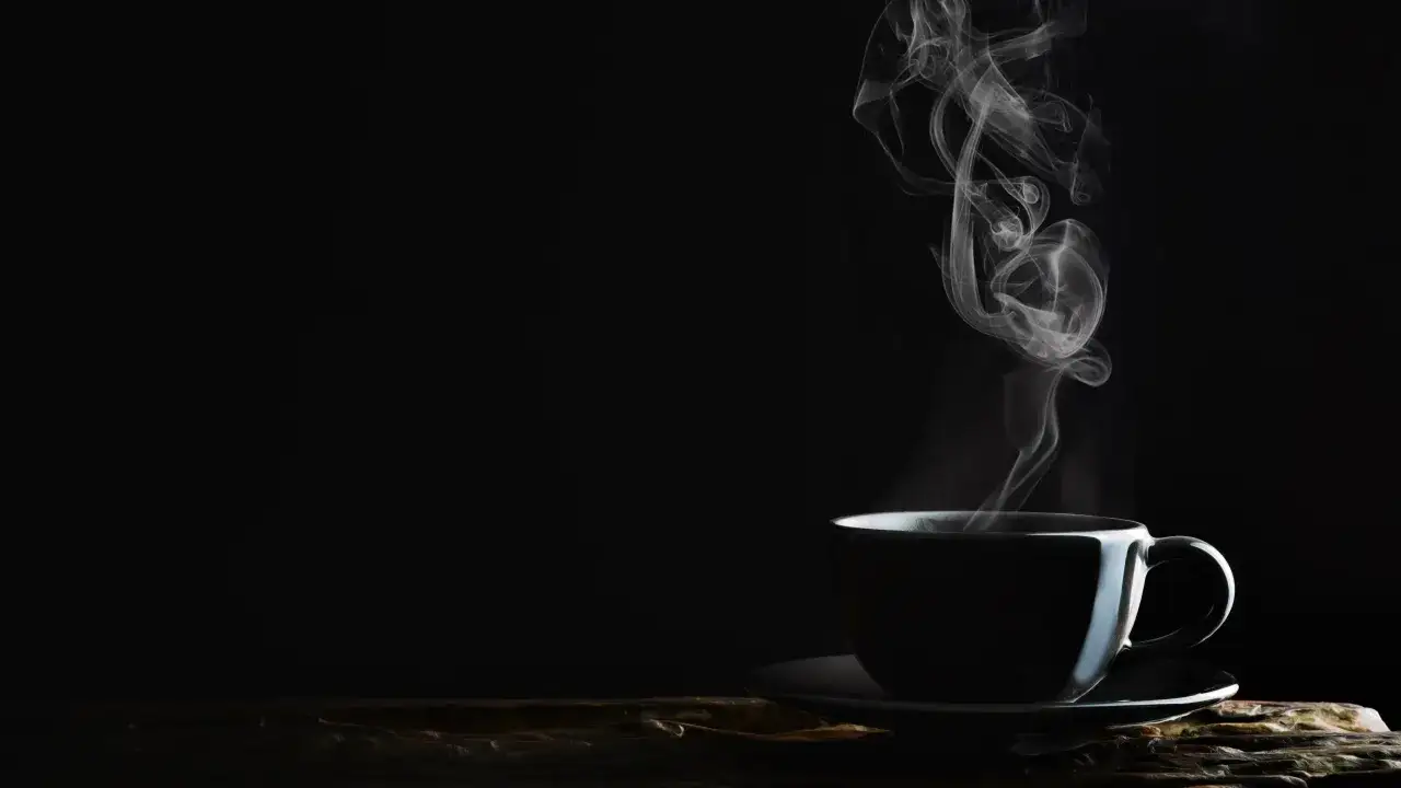 Dampfender, koffeinfreier Kaffee bei Bluthochdruck. Eine Tasse auf einem Unterteller, vor schwarzem Hintergrund.