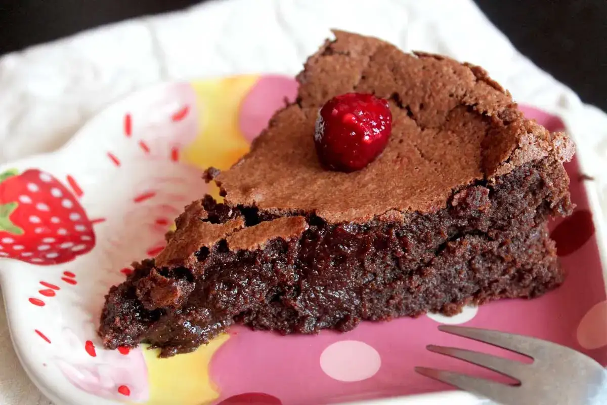 Deliciosa tarta de chocolate sin gluten y sin lactosa, coronada con una frambuesa, servida en un plato con fresas.