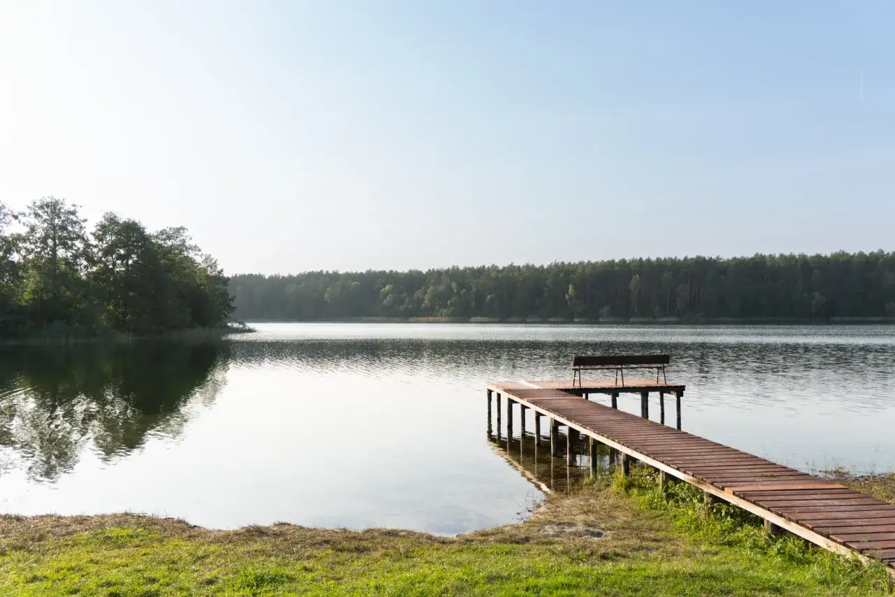 Drewniane molo z ławką nad spokojnym jeziorem Ostrowite w Kujawsko-Pomorskiem, otoczone zielenią.