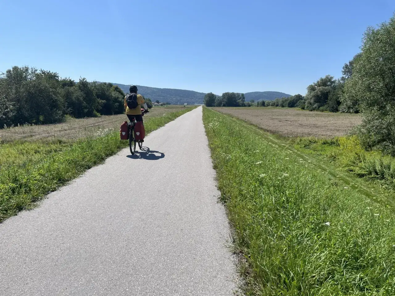 Rowerzysta przemierza malownicze **jezioro rożnowskie trasy rowerowe**. Słoneczny dzień sprzyja podr&oacute;ży przez zielone pola i lasy.