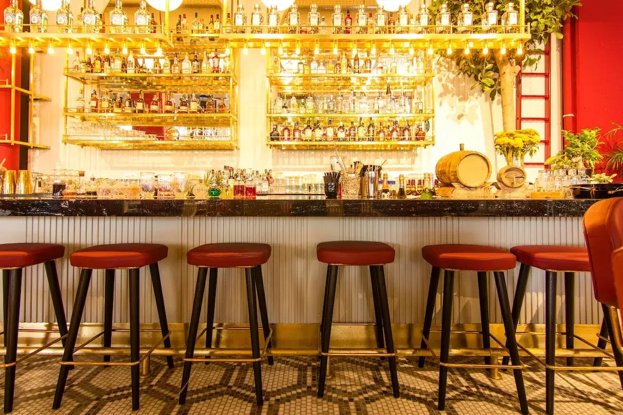 Bar con botellas doradas y taburetes rojos. Ideas para decorar un bar con poco dinero: ¡la iluminación y los detalles marcan la diferencia!