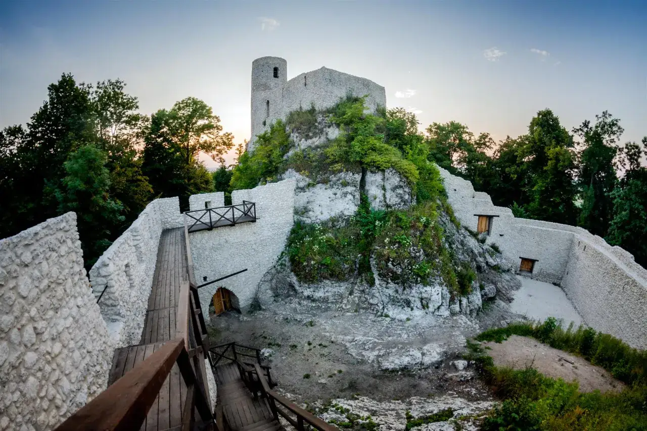 Kamienne mury i wieża zamku Pilcza w Smoleniu, otoczone zielenią, z drewnianymi schodami prowadzącymi do ruin.