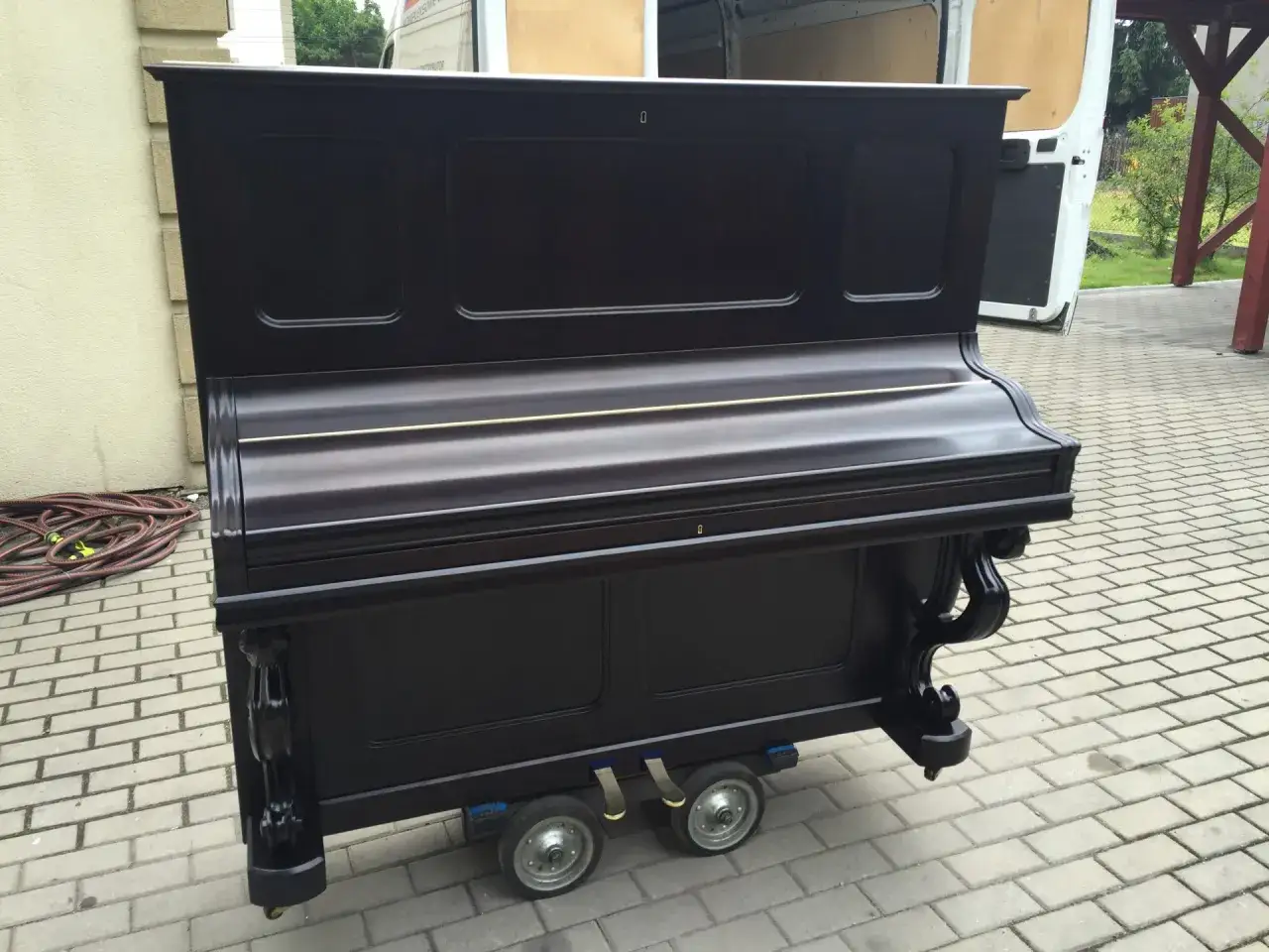Ciemnobrązowe pianino pionowe na wózeczku z kółkami, gotowe do transportu. Zastanawiasz się, ile waży pianino? To ciężki instrument!