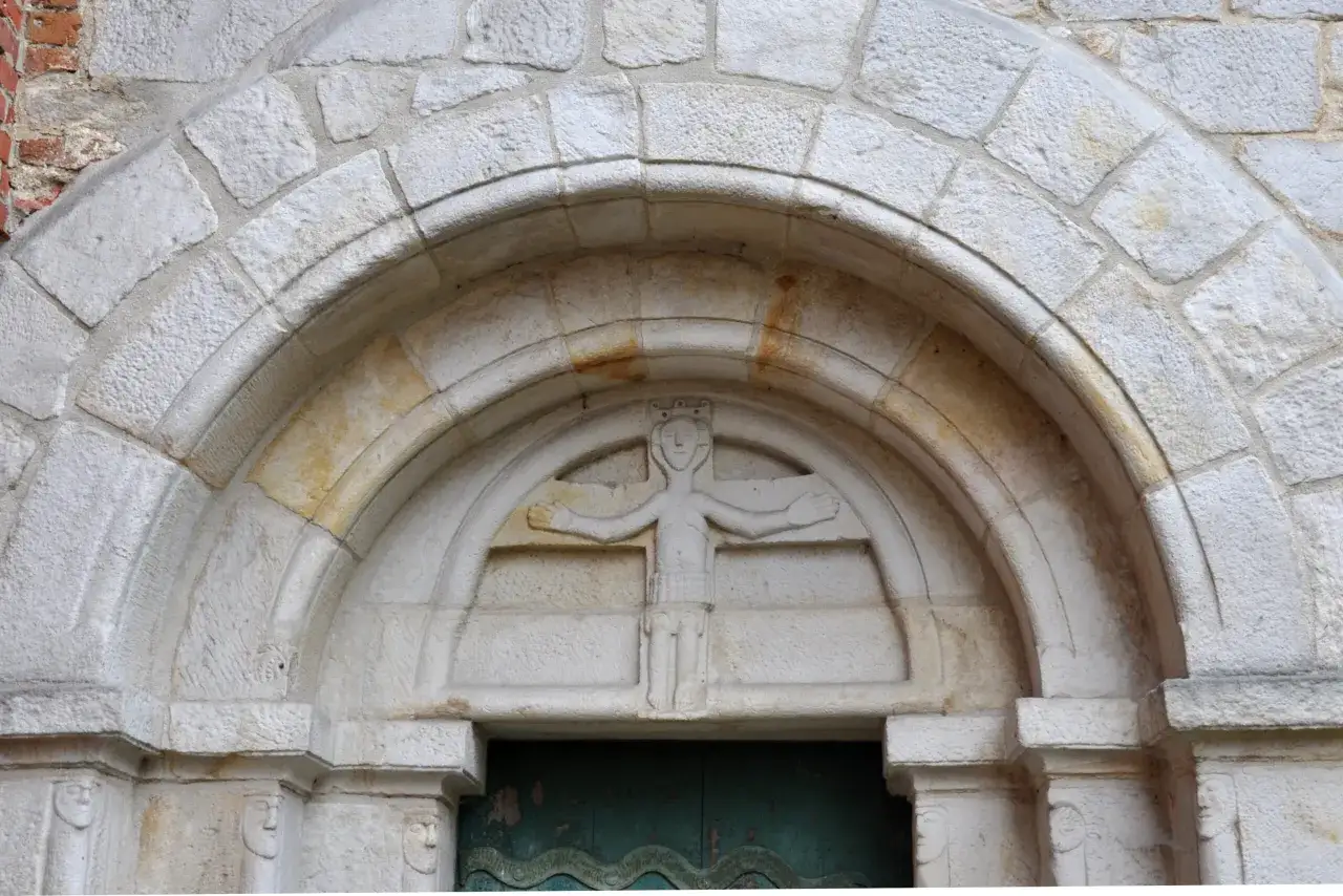 Kamienna rzeźba postaci ludzkiej z koroną na głowie, ozdabiająca portal. Charakterystyczne dla sztuki romańskiej detale architektoniczne.