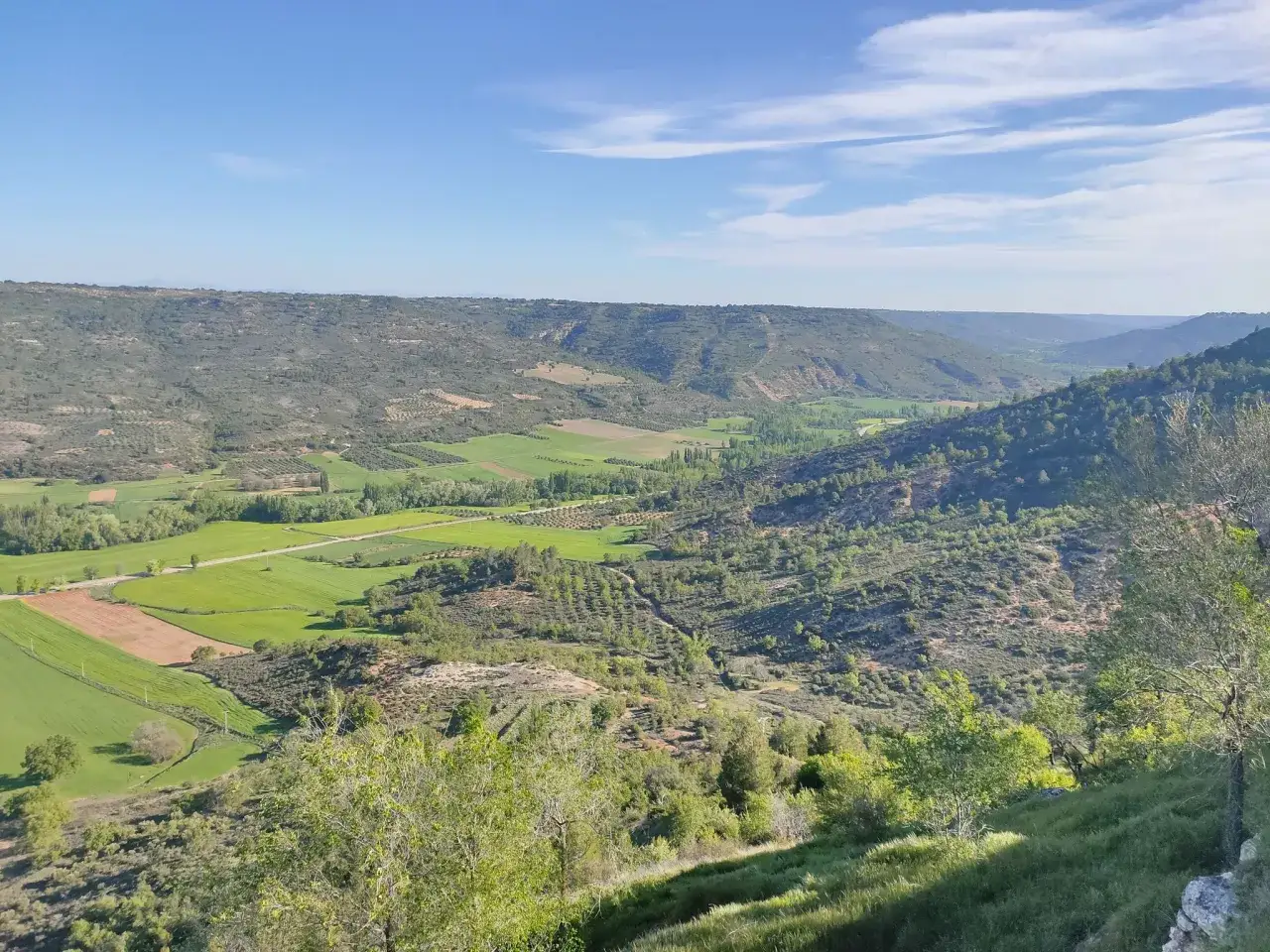 Vistas verdes y onduladas desde el balc&oacute;n de Taju&ntilde;a, con campos cultivados y colinas cubiertas de vegetaci&oacute;n bajo un cielo azul.