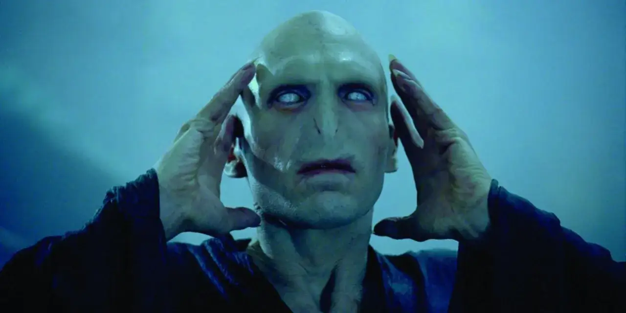 Ralph Fiennes jako Voldemort w Harry Potterze, z dłońmi przy skroniach, wpatruje się w mrok.