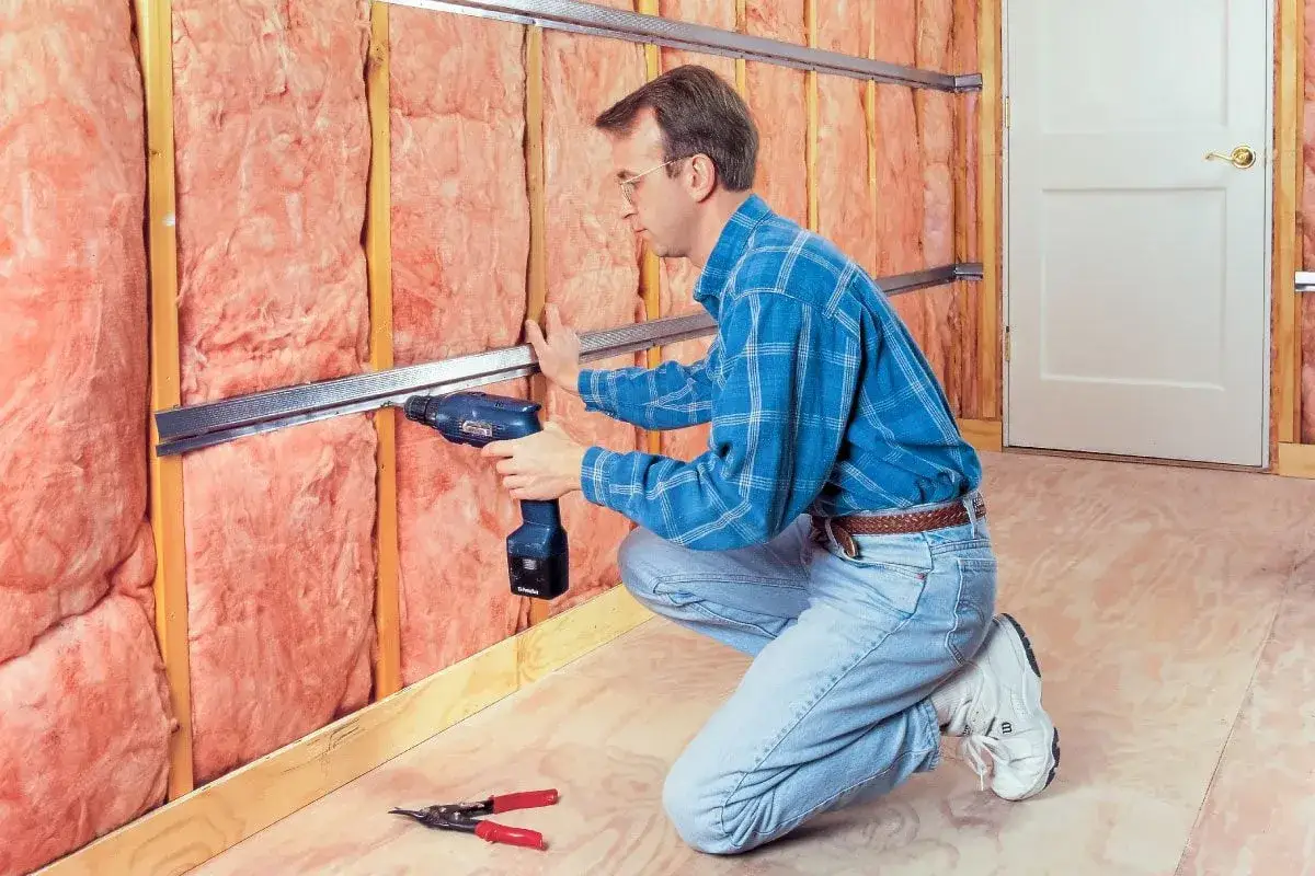Hombre instala perfiles met&aacute;licos para insonorizar habitaci&oacute;n con aislamiento rosa.