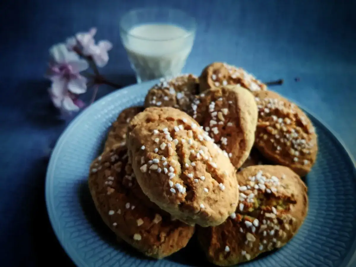 En tallrik med mandelkubbar, perfekta för ett mandelkubb recept. En glas mjölk och en blommande kvist i bakgrunden.