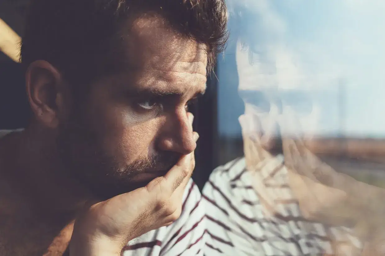 Viso di un uomo pensieroso, con la mano sul mento, riflesso nel vetro. Un'espressione di profonda tristezza, il volto di un depresso.