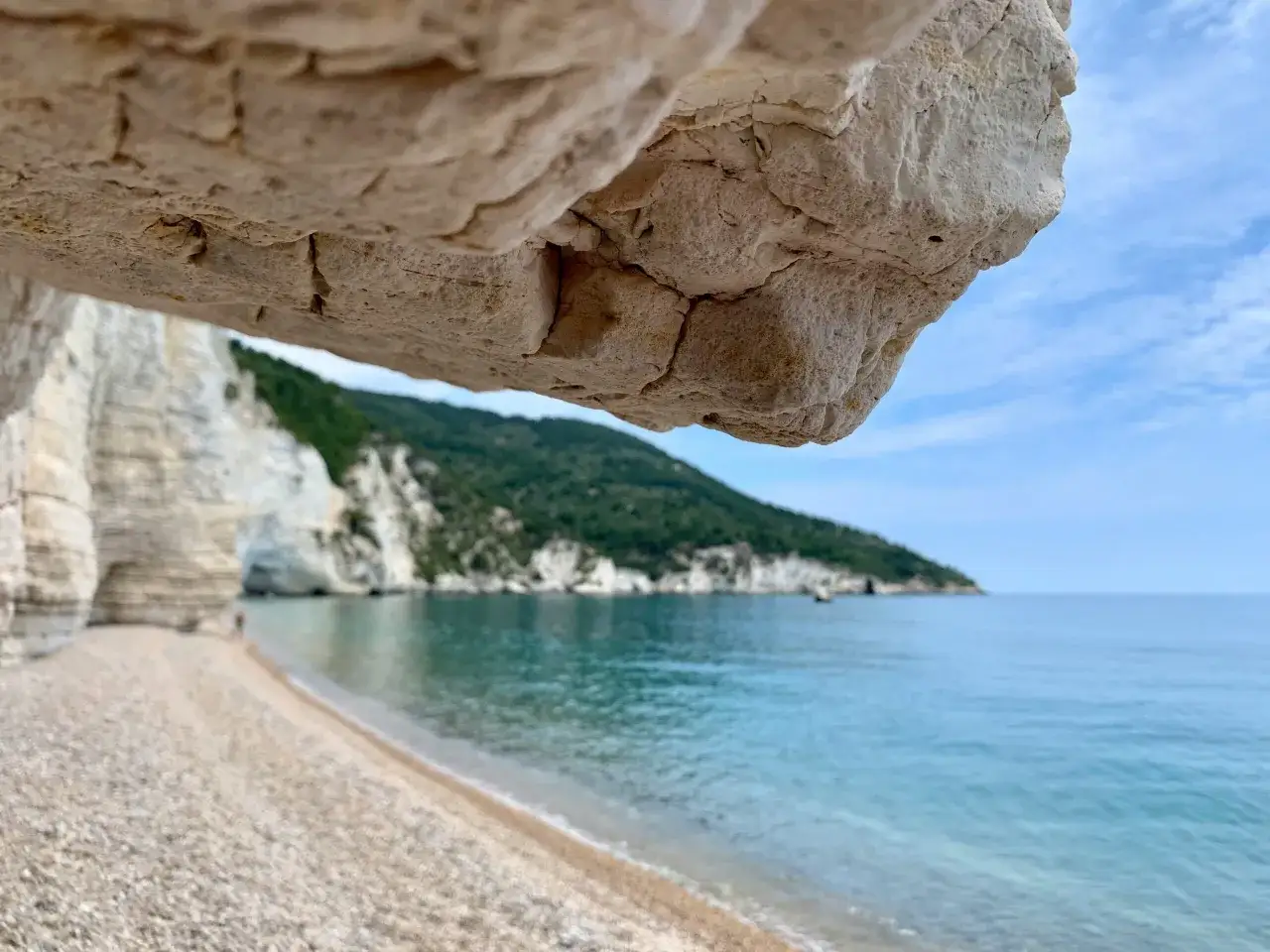 Vue depuis une grotte sur une plage de galets, avec des falaises blanches et une mer bleue sur la côte adriatique Italie.