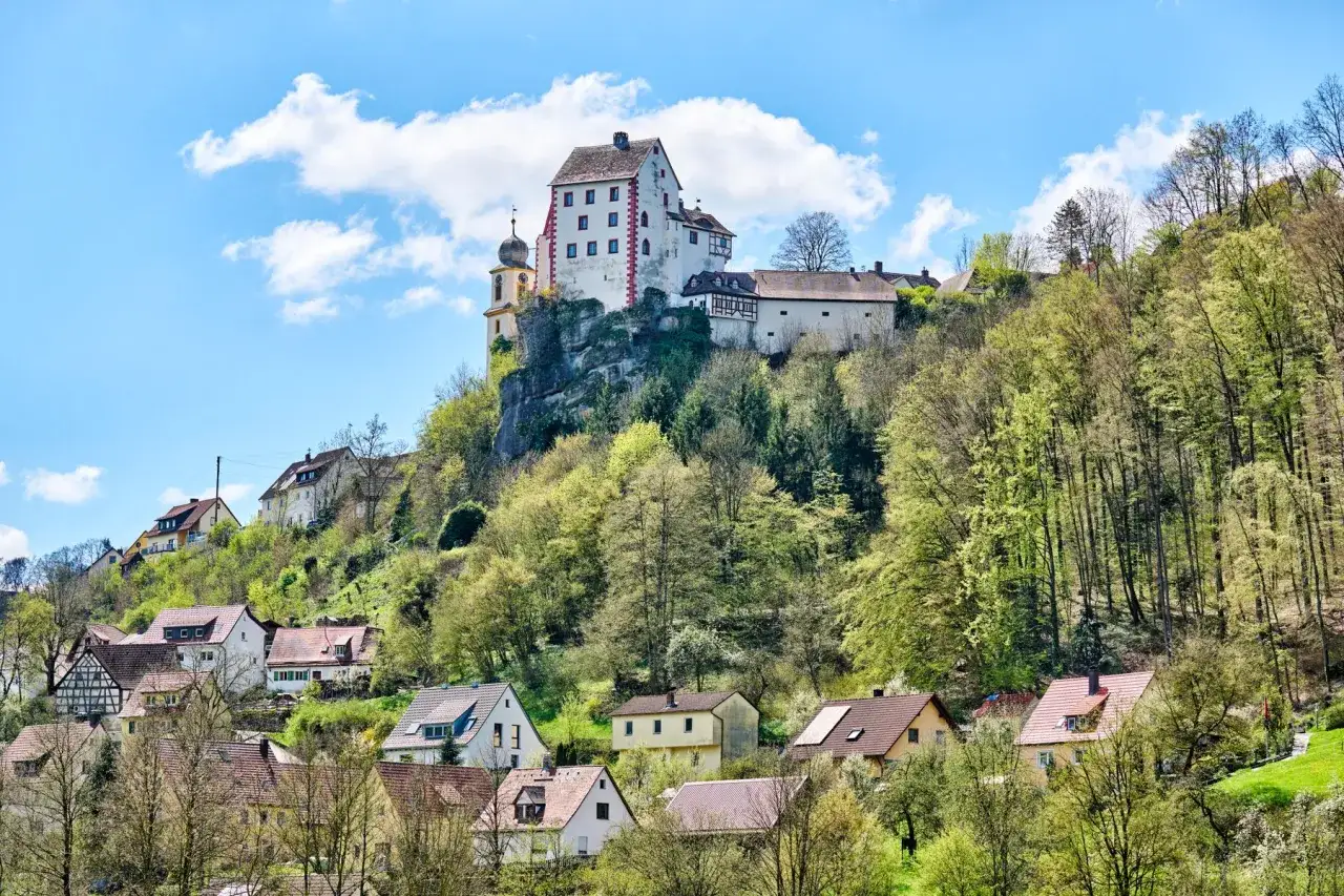 Burg und Dorf von Egloffstein thronen auf einem Felsen, umgeben von gr&uuml;nen W&auml;ldern und bl&uuml;hendem Fr&uuml;hling.