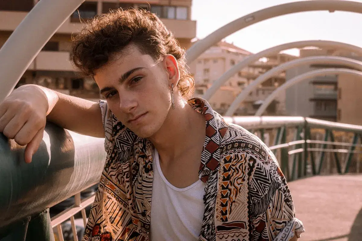 Joven con un moderno mullet y camisa estampada, apoyado en una barandilla.