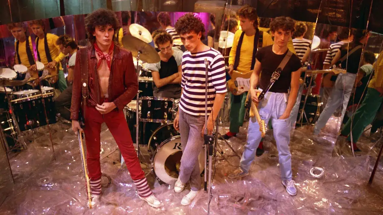 Zespół Lady Pank w latach 80. na scenie, w kolorowych strojach, z gitarami i perkusją.