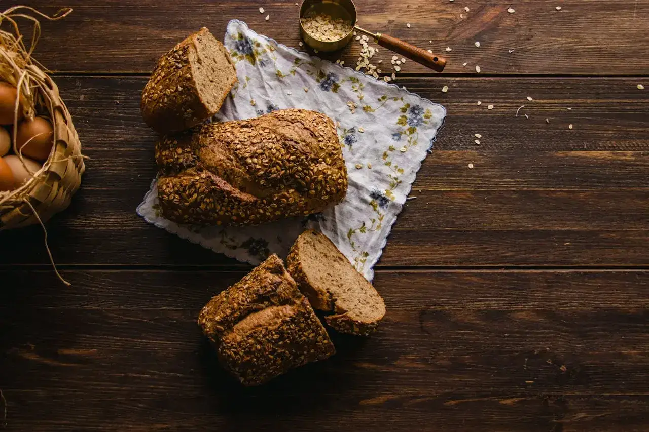 Frisch gebackenes Haferbrot, ein Teil davon angeschnitten, liegt auf einem gemusterten Tuch. Daneben ein Korb mit Eiern und eine Schale mit Haferflocken. Ein köstliches Haferbrot Rezept!