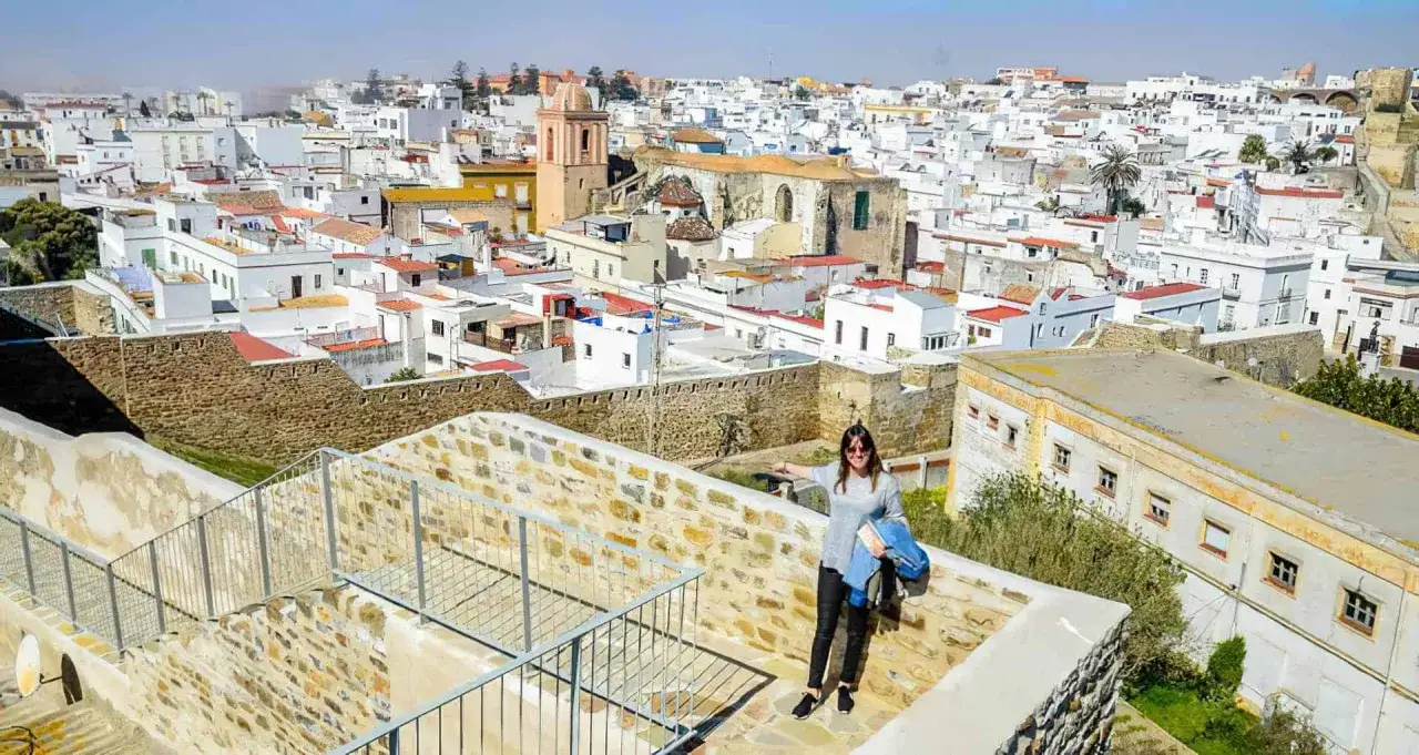Una mujer sonríe en un balcón con vistas a las casas blancas de Tarifa. ¡Un lugar perfecto para descubrir qué hacer en Tarifa!