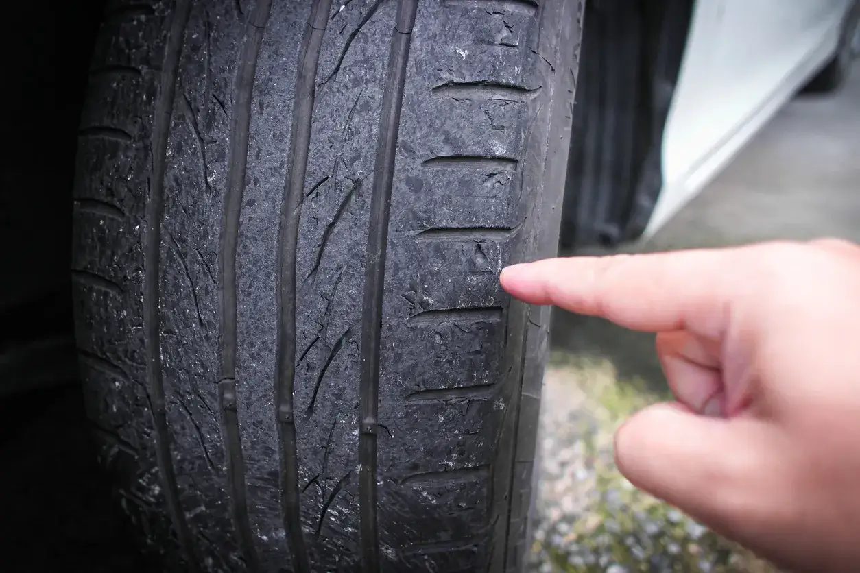 Doigt pointant un pneu usé, signe d'un possible problème de prix d'une géométrie voiture.