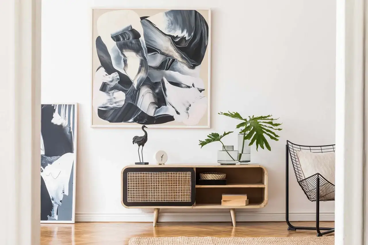 Come valorizzare una parete vuota con un mobile basso in legno, quadri astratti e una sedia di design.