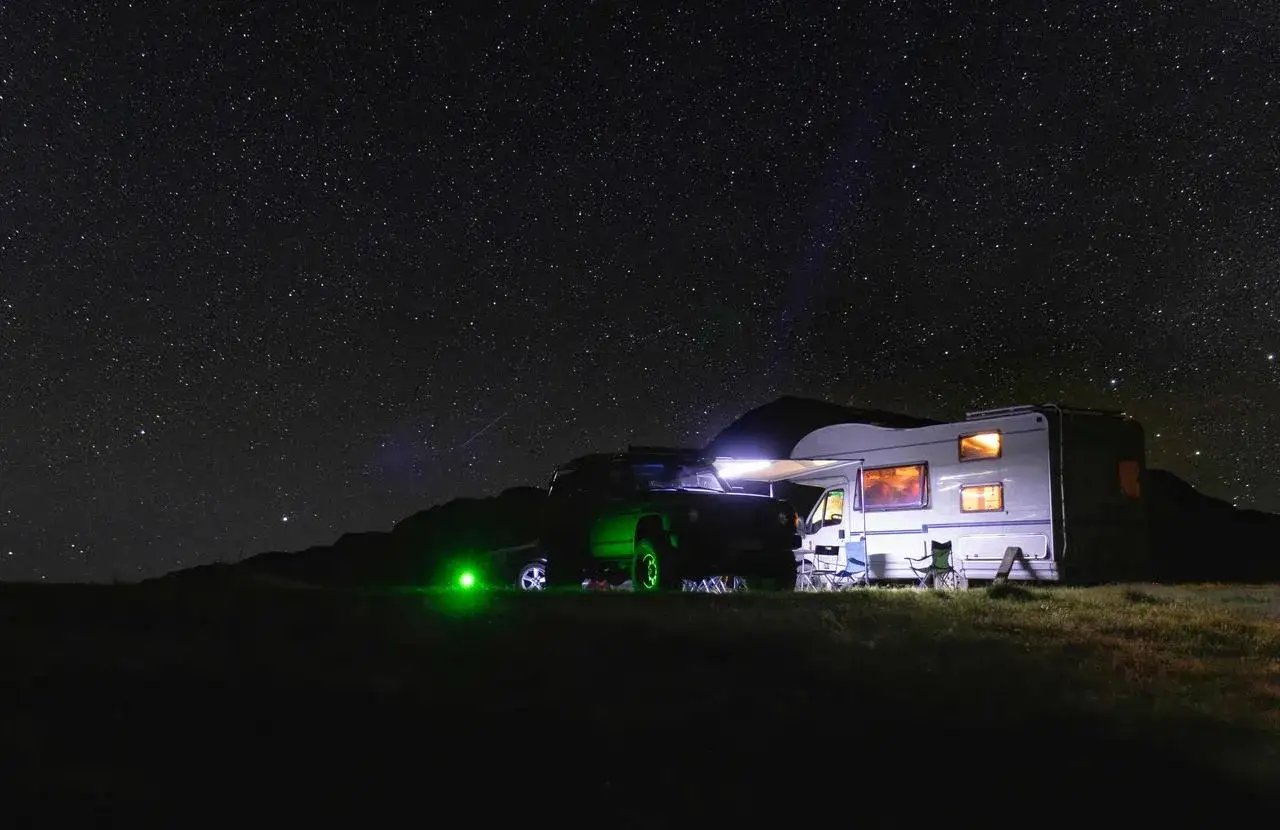 Un camping-car et un 4x4 illuminés sous un ciel étoilé. L'endroit idéal où dormir en camping-car pour admirer la voie lactée.