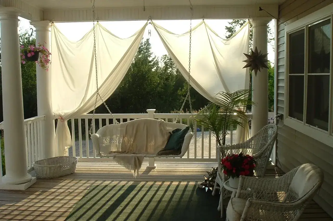 Un portico accogliente con altalena, sedie in vimini e tende leggere: idee per come abbellire un portico con stile e comfort.