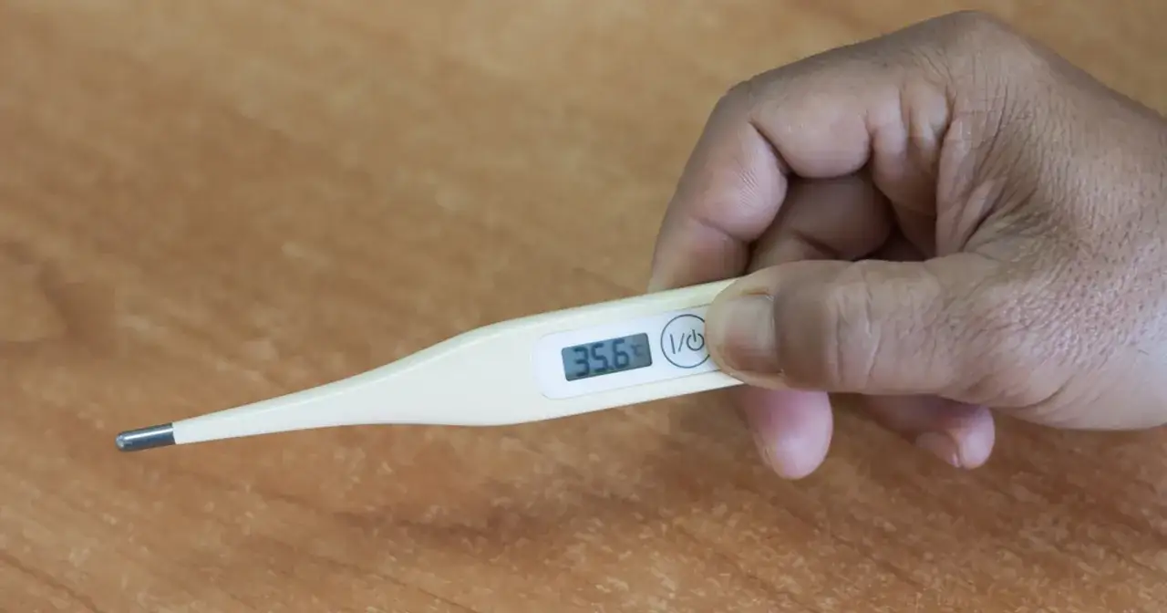 Dłoń trzyma termometr pokazujący 35.6°C. Czy to objaw niskiej temperatury przy covid?