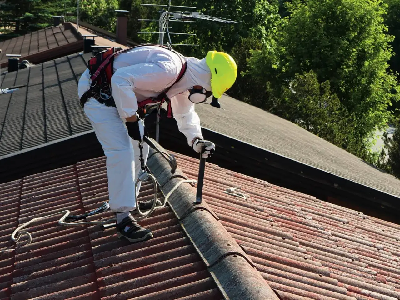 Pracownik w kombinezonie i kasku na dachu, przygotowujący się do prac. Może to być etap przed uzyskaniem dotacji na wymianę dachu.