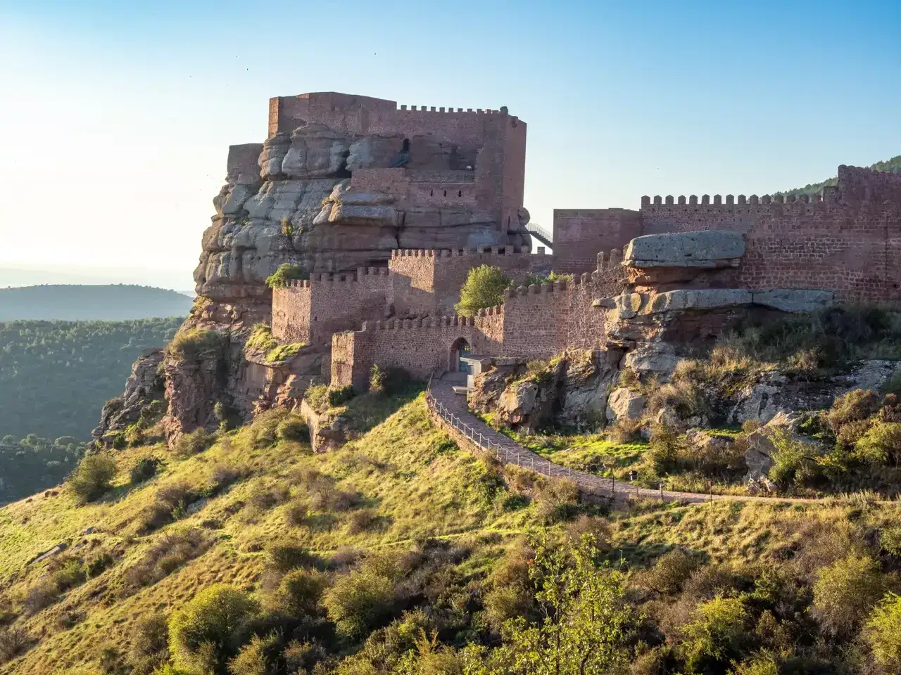 El imponente castillo de Peracense se alza sobre un pe&ntilde;&oacute;n rocoso, con murallas de piedra rojiza y un camino serpenteante que invita a explorarlo.
