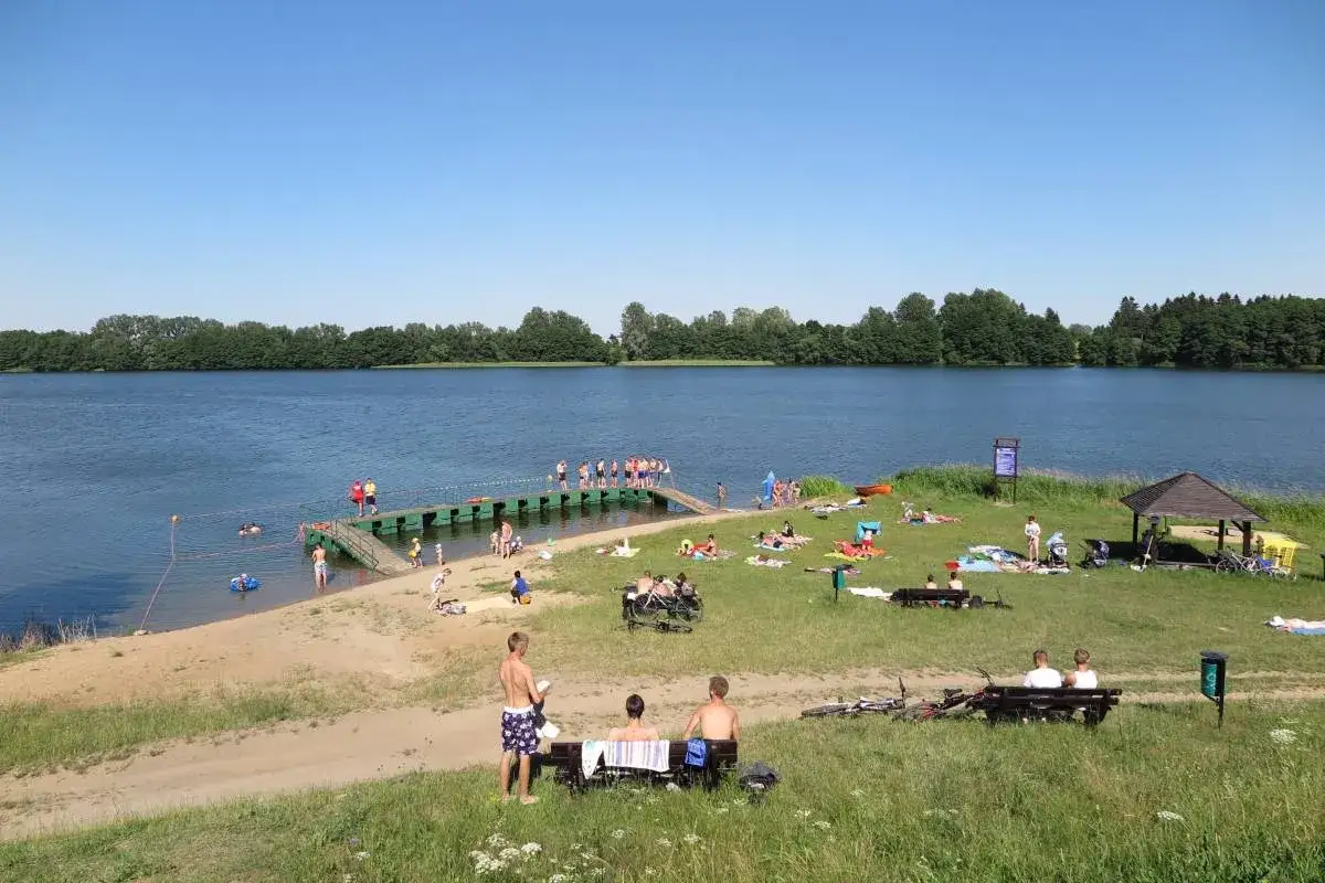 Słoneczny dzień nad **czaplinek jezioro**. Ludzie odpoczywają na plaży, kąpią się i opalają.