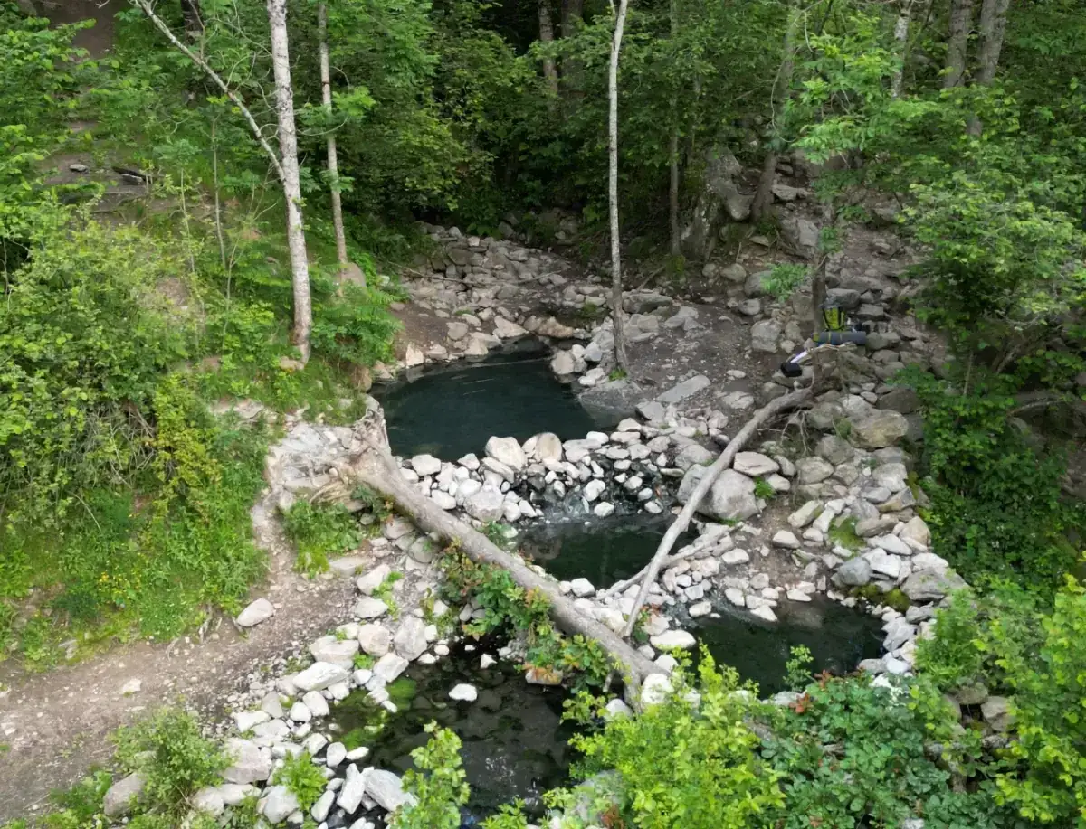 Baignade naturelle dans les eaux chaudes de Merens-les-Vals, au cœur d'une forêt luxuriante. Un randonneur s'apprête à profiter de ce havre de paix.