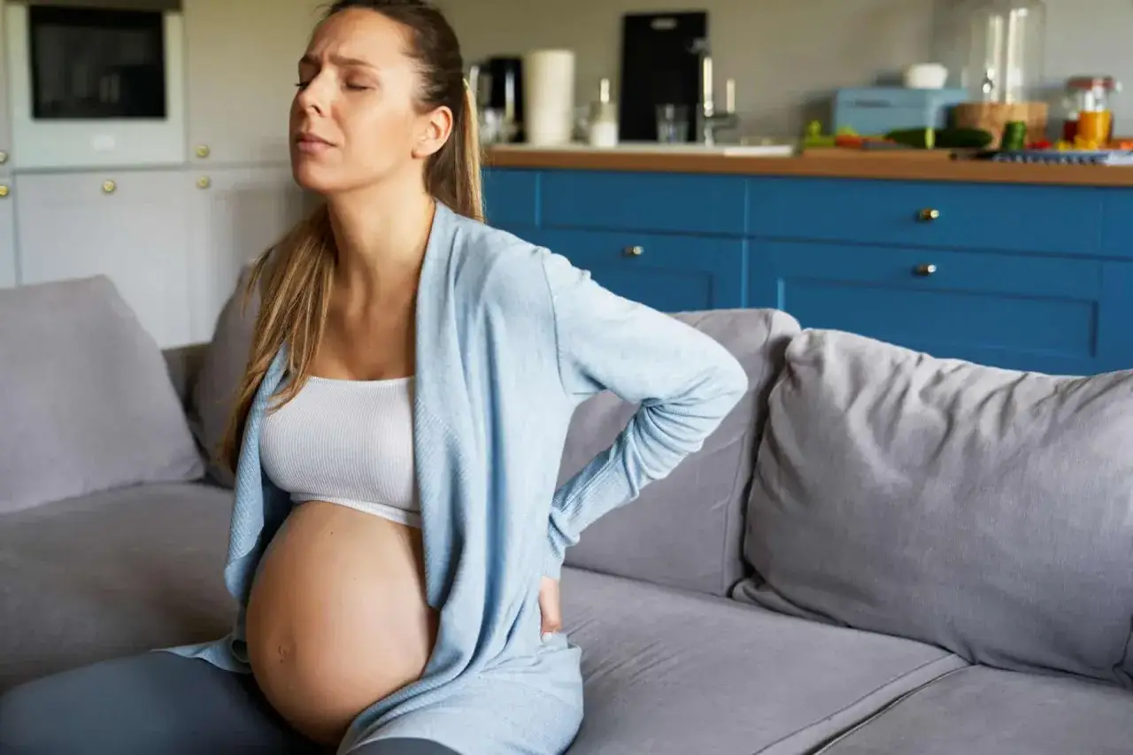 Schwangere Frau mit R&uuml;ckenschmerzen auf dem Sofa. Sie fragt sich, wann die Wehen beginnen und sie ins Krankenhaus muss.