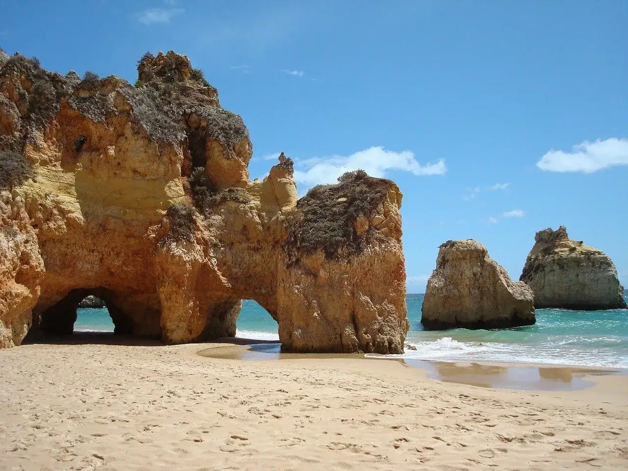 Playa dorada en el Algarve, ideal para disfrutar con niños. Rocas ocre con arcos naturales y mar turquesa.