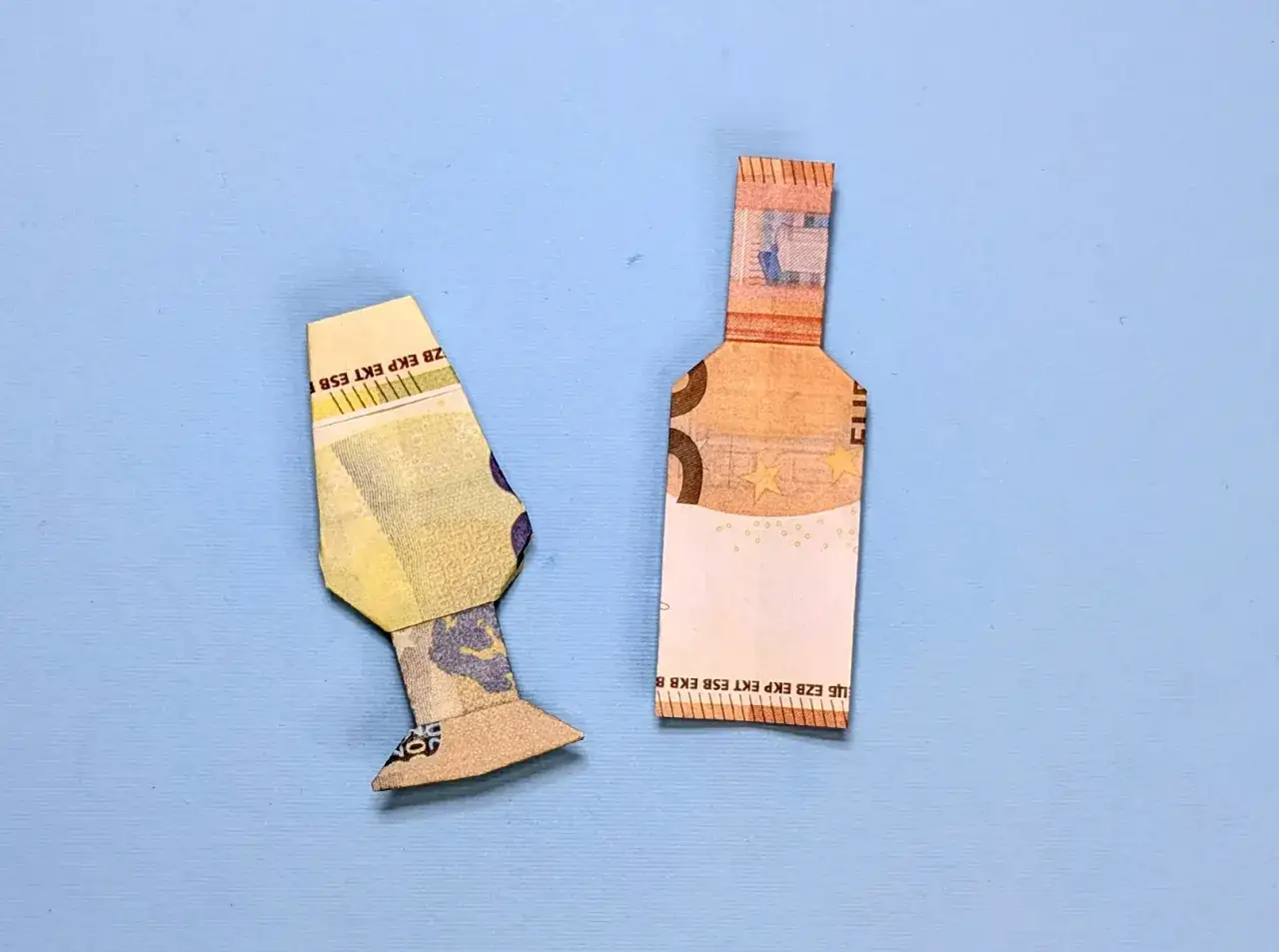 Zwei gefaltete Euroscheine, die eine Flasche und eine Art Vase darstellen. Geld falten flasche als kreative Deko.