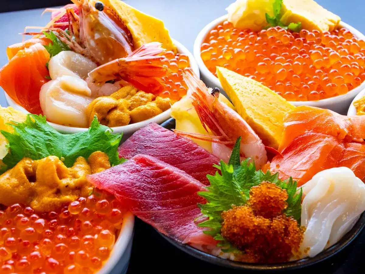 A vibrant spread of Hokkaido food: fresh salmon, tuna, uni, ikura, scallops, shrimp, and tamagoyaki served over rice.