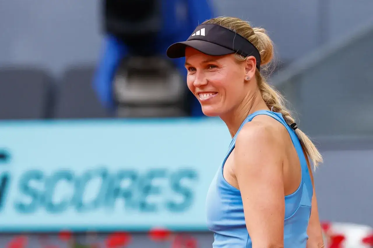 Uśmiechnięta duńska tenisistka polskiego pochodzenia, Caroline Wozniacki, w niebieskim stroju sportowym i czarnej czapce z daszkiem.
