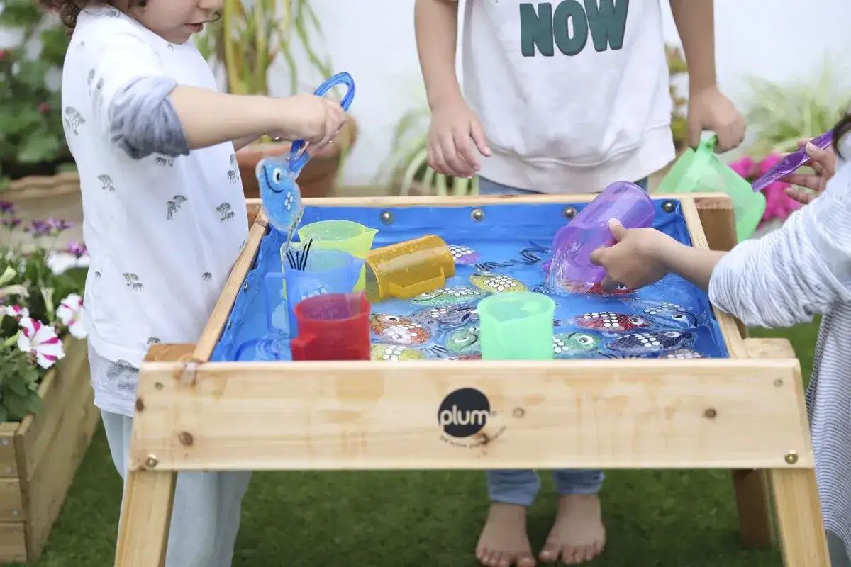 Niños jugando con peces de juguete en una mesa de agua, como si estuvieran en la playa.