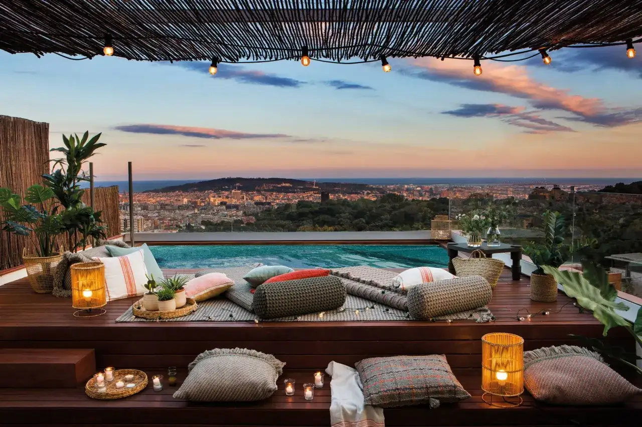 Rel&aacute;jate junto a las piscinas en &aacute;ticos con vistas panor&aacute;micas al atardecer. Cojines, velas y luces crean un ambiente acogedor.