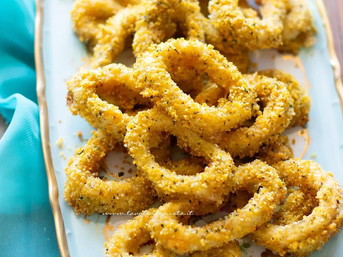 Anelli di totano al forno, dorati e croccanti, serviti su un piatto azzurro con un tovagliolo turchese.