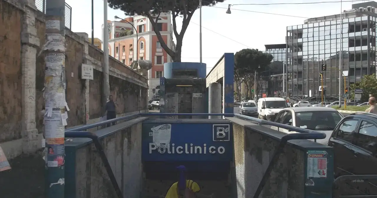Ingresso della metro B Policlinico, con edifici moderni e alberi sullo sfondo. Traffico in strada.