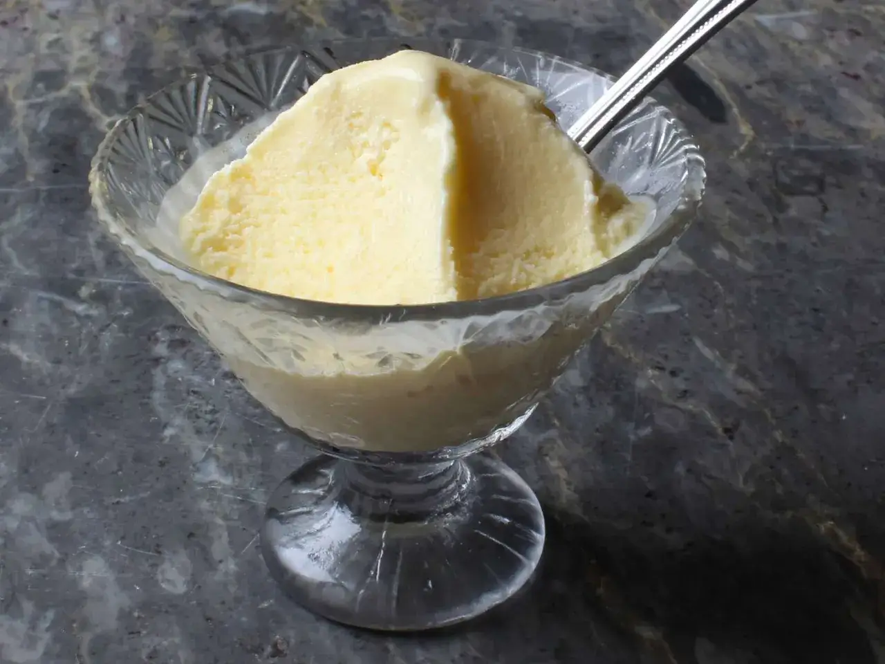 Cremiges Vanilleeis in einer Glasschale, das an ein original italienisches Eis Rezept erinnert. Ein L&ouml;ffel steckt darin.