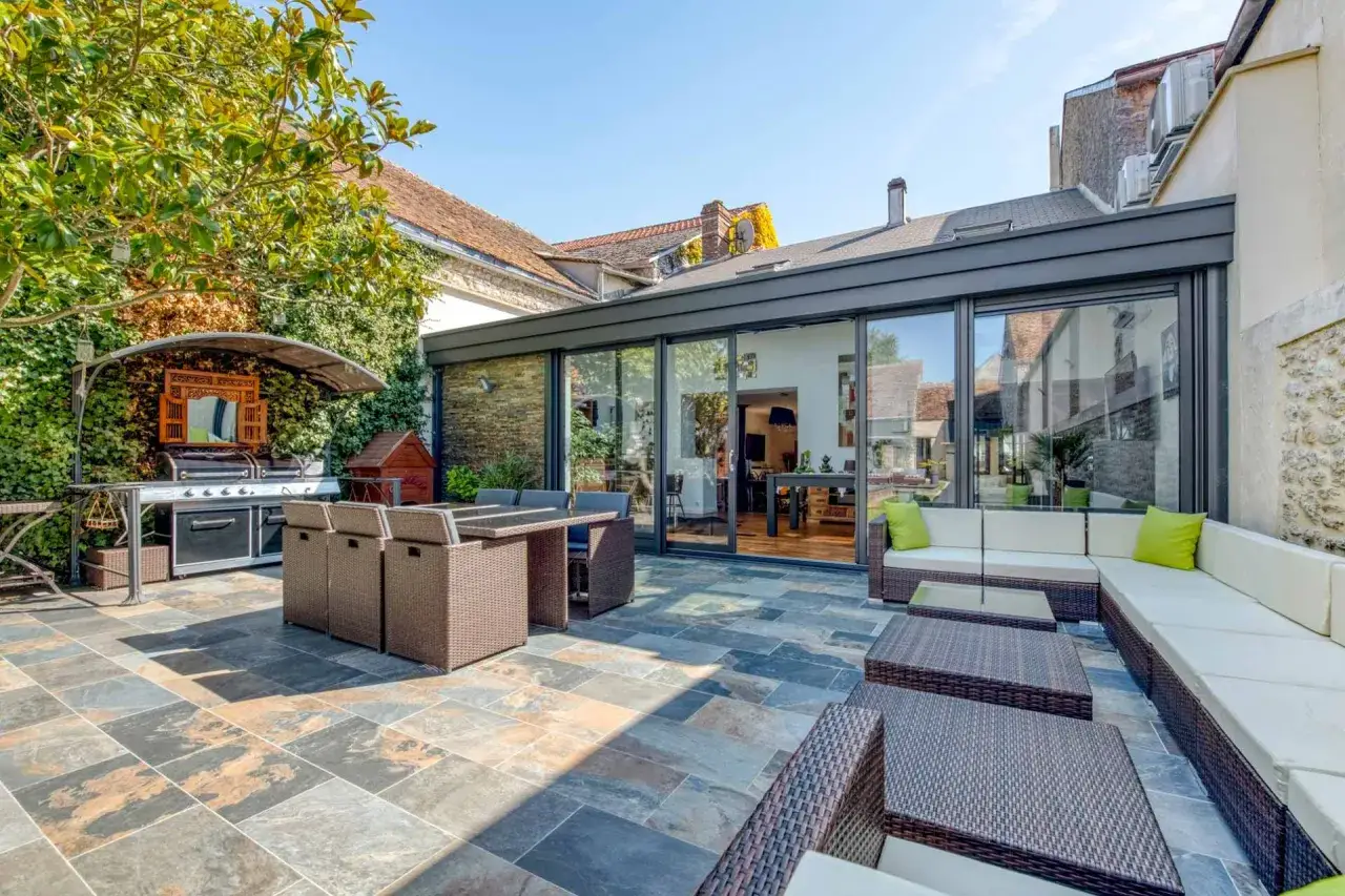 Terrasse moderne avec salon de jardin, barbecue et extension de maison. L'extension permis de construire a créé un espace de vie lumineux.