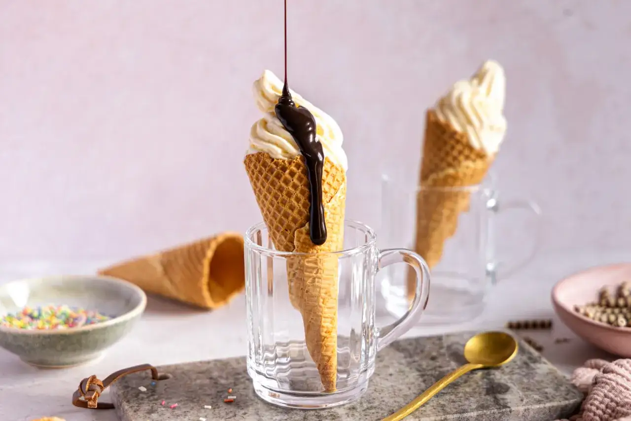 So much fun to softeis selber machen! Ein Eis im Waffelhörnchen wird mit Schokoladensauce übergossen, bereit zum Genießen.