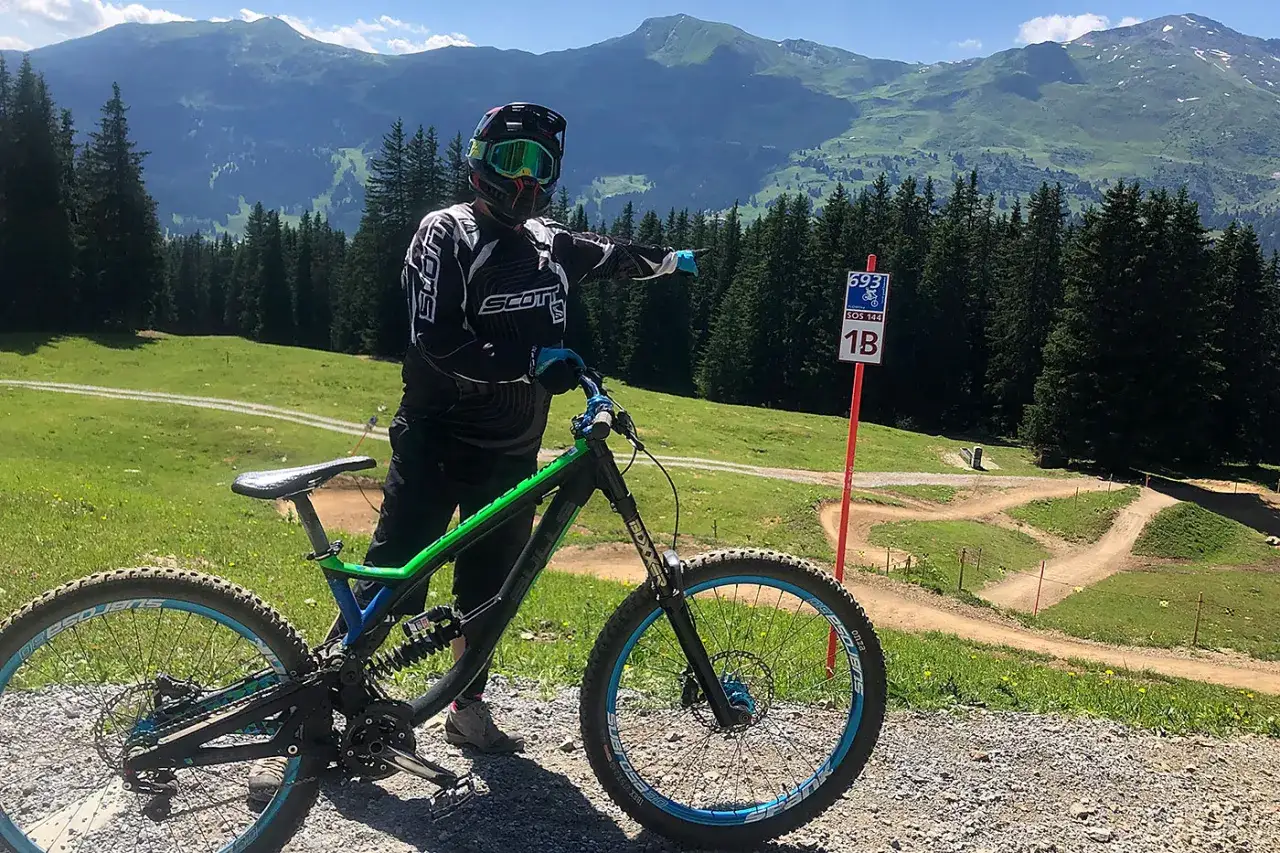 Rowerzysta w kasku i goglach wskazuje drogę na trasie zjazdowej. To właśnie jest downhill – ekstremalna jazda rowerem po górskich ścieżkach.