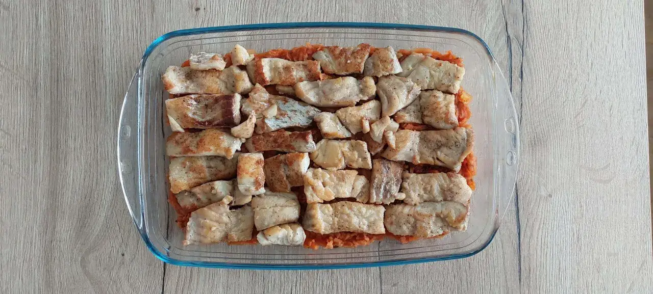 Keto ryba po grecku w naczyniu żaroodpornym, ułożona na warzywach.